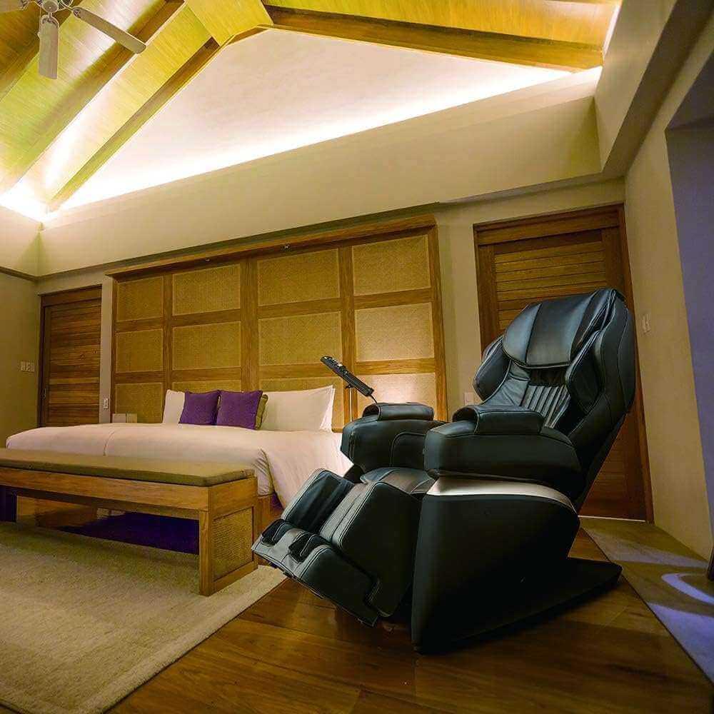 Synca Wellness Kurodo Massage Chair in black leather positioned in a cozy modern bedroom