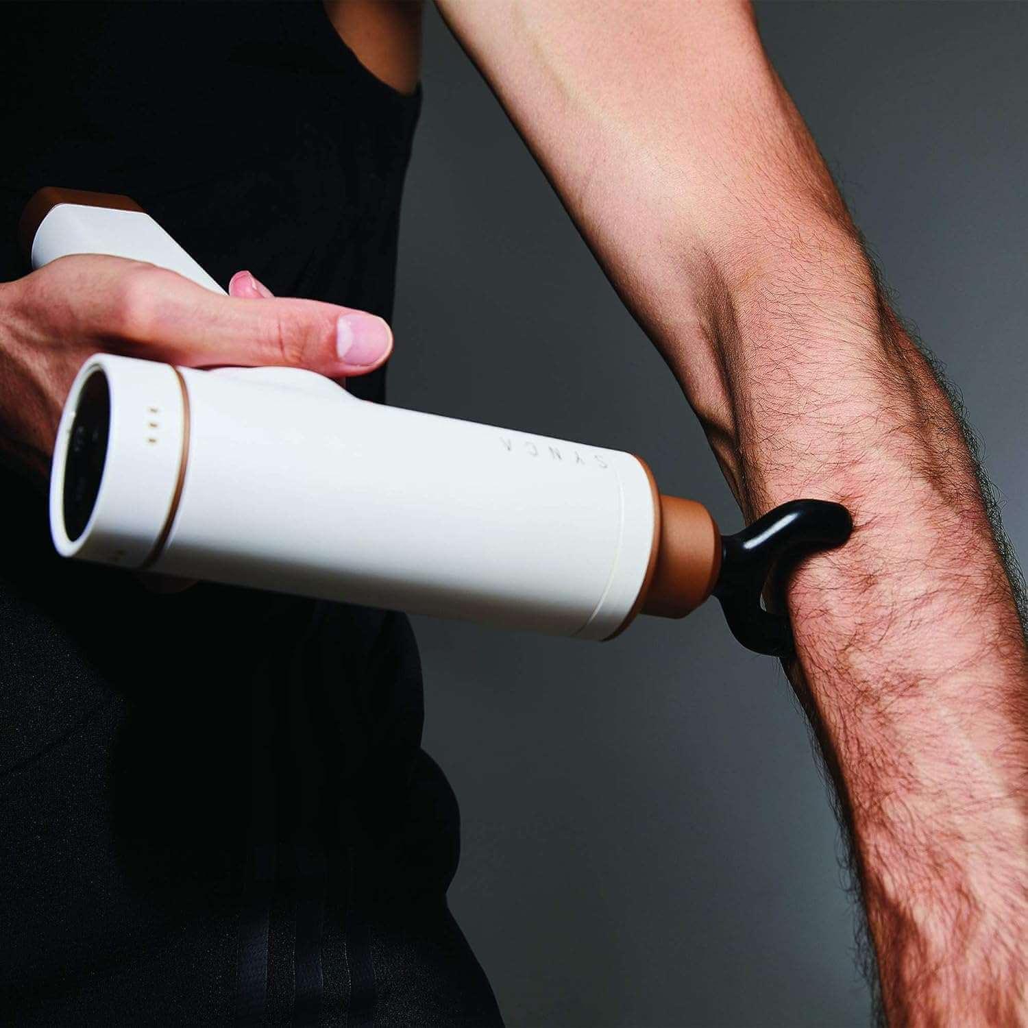 Synca Wellness white percussive massage gun being used on forearm muscles for deep muscle relief