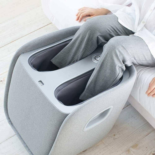 Masajeador de pies Synca Wellness REI en tela gris con persona usándolo en los pies mientras está sentada