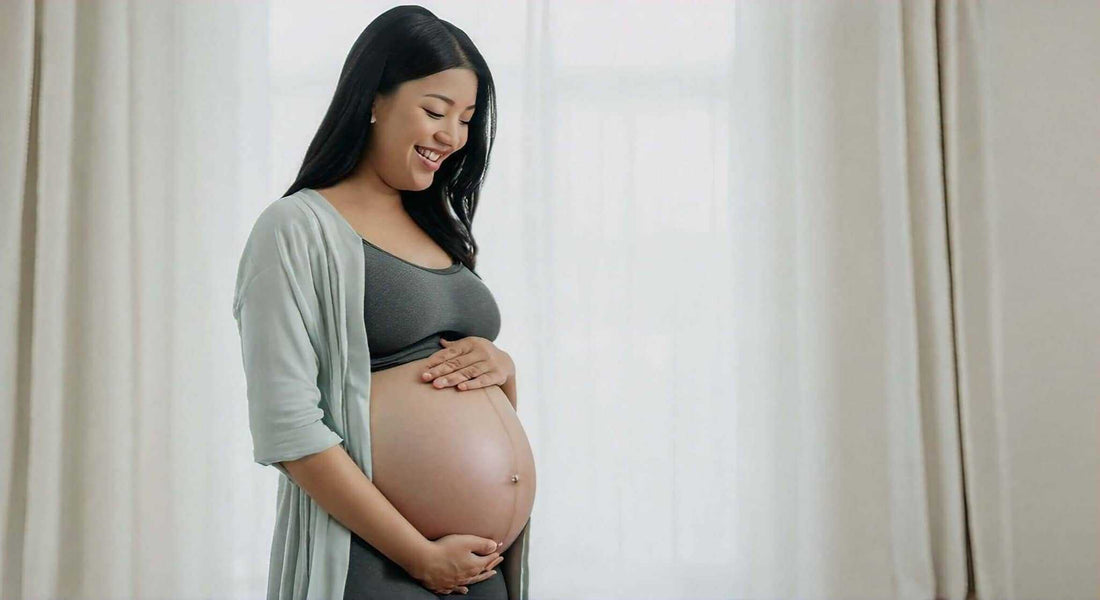 Pregnant woman in a gray top and light cardigan cradles her belly; Are Massage Chairs Safe During Pregnancy?