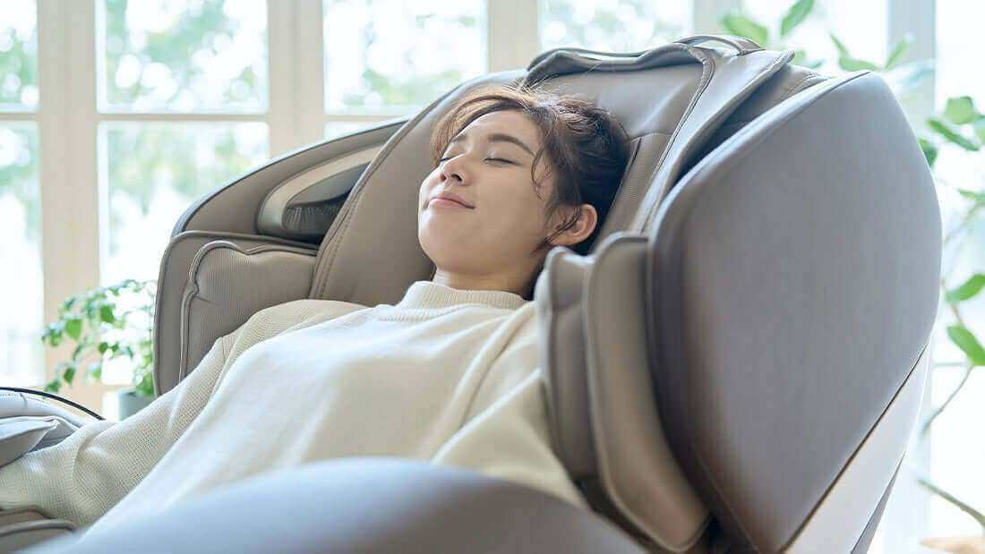 Gray massage chair with padded side panels cradles a relaxed woman reclining in a white robe; Experience Ultimate Relaxation: How Fujiiryoki Calm Plus Massage Chair Enhances Blood Flow and Relieves Fatigue