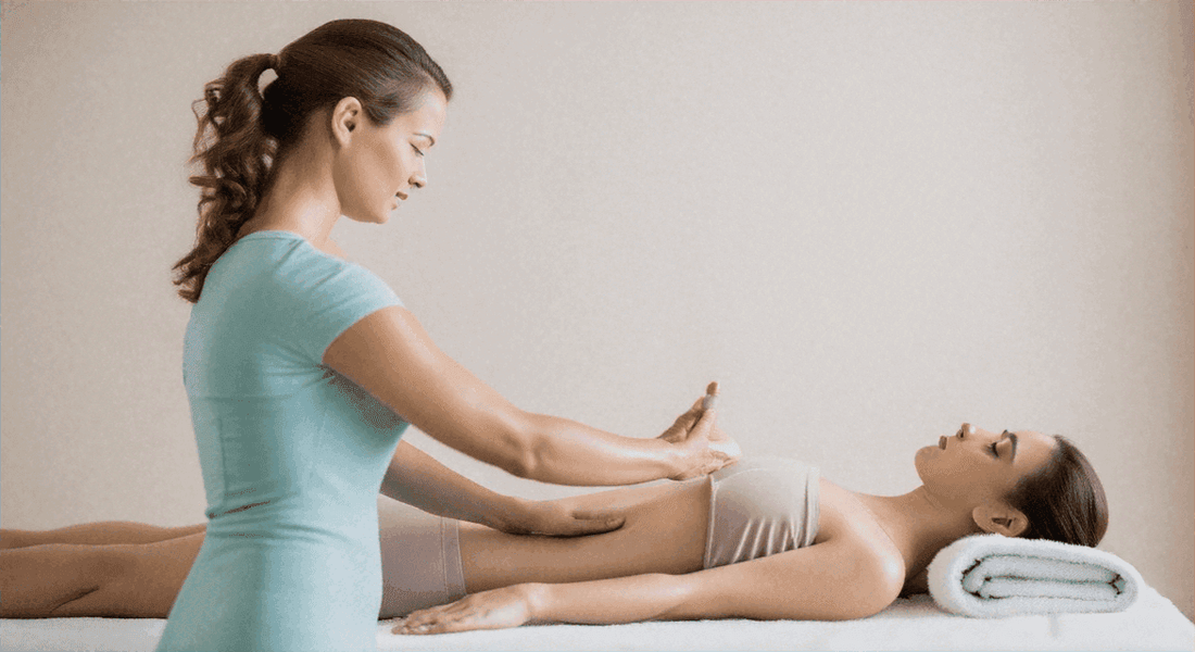 Wellness treatment with therapist in turquoise uniform pressing an acupressure point on a reclining woman's abdomen