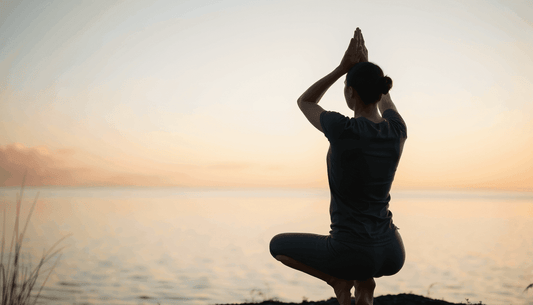 Yoga meditation for Tension Headaches, showing a person in dark clothing balancing in a seated pose with palms pressed overhead.