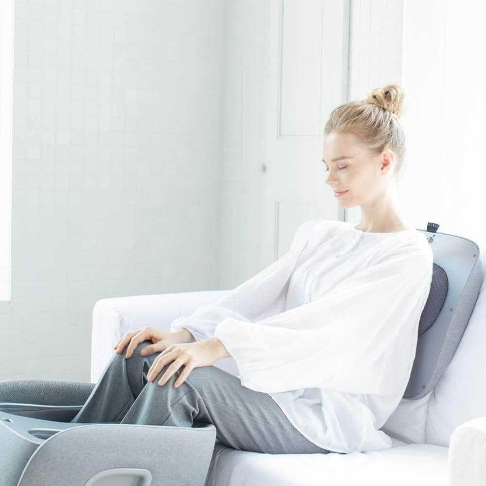 Foot + Calf + Lumbar Ottoman Massager in light gray with a fabric-covered foot compartment and a woman seated using it