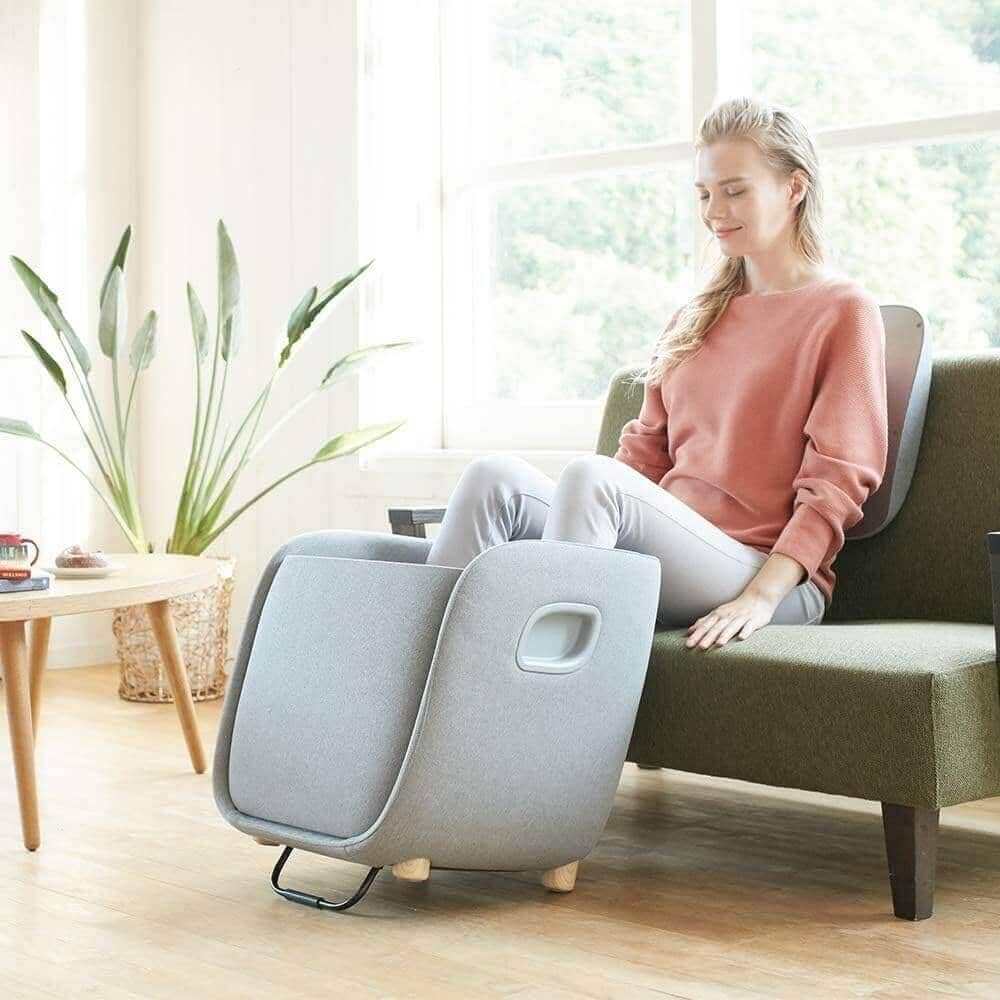 Foot + Calf + Lumbar Ottoman Massager in light gray fabric with padded foot compartments and a woman seated using it