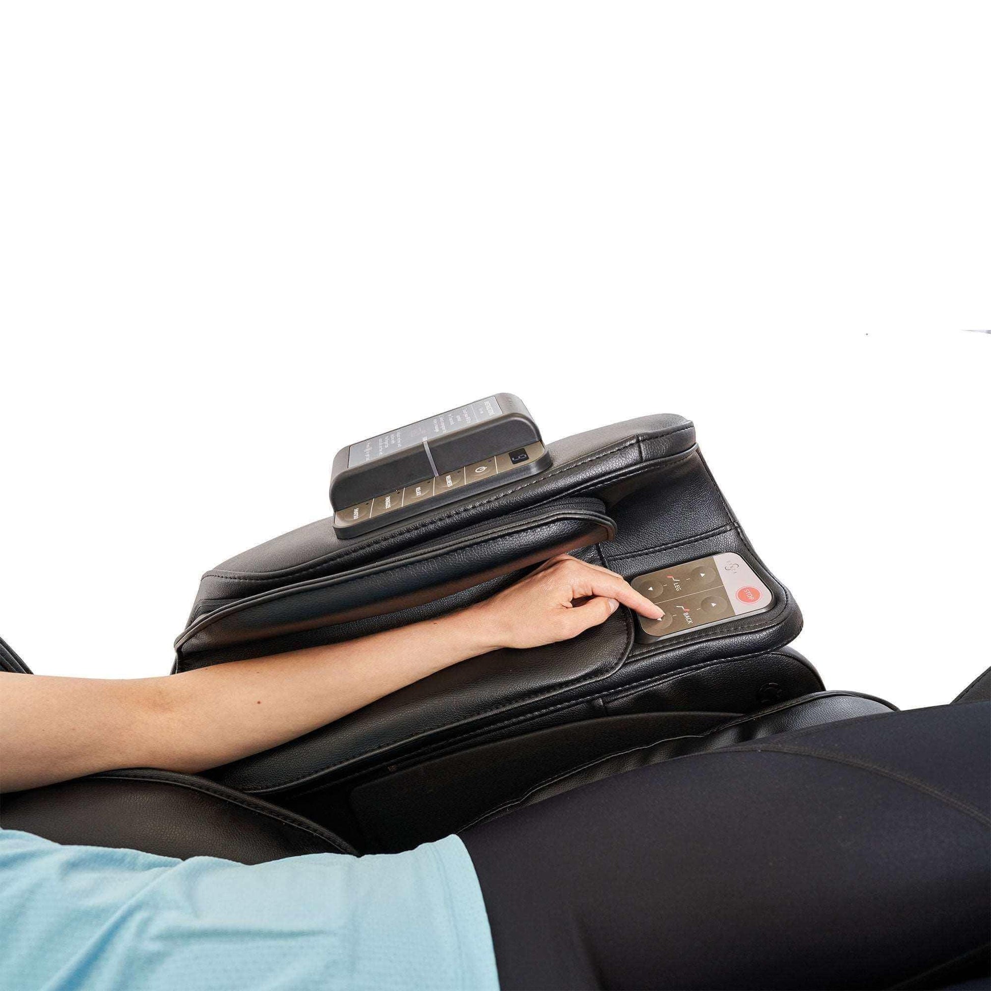 Person using Synca Wellness commercial massage chair with remote control on black leather armrest