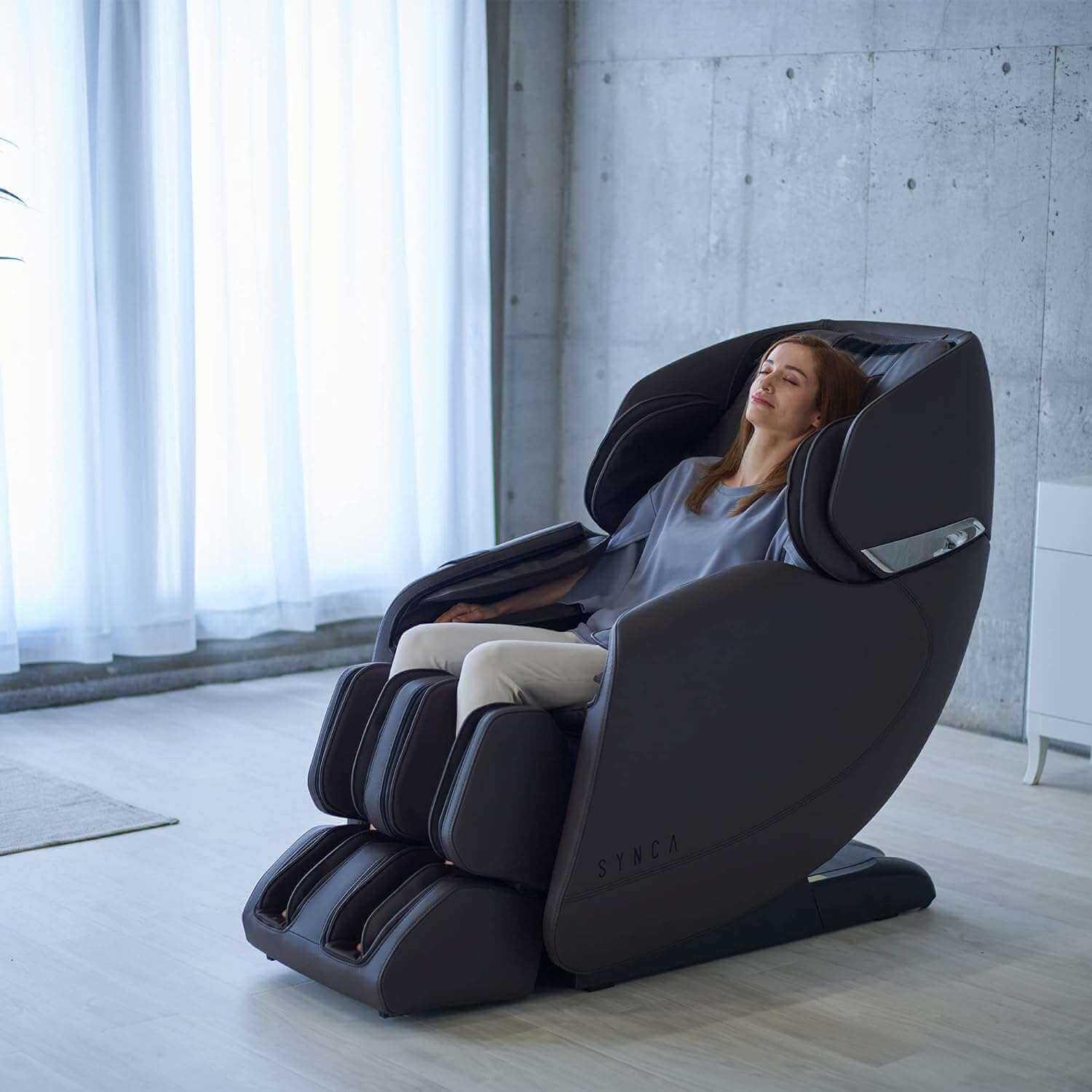 Synca Wellness Hisho massage chair in black with a woman relaxing in a modern living room