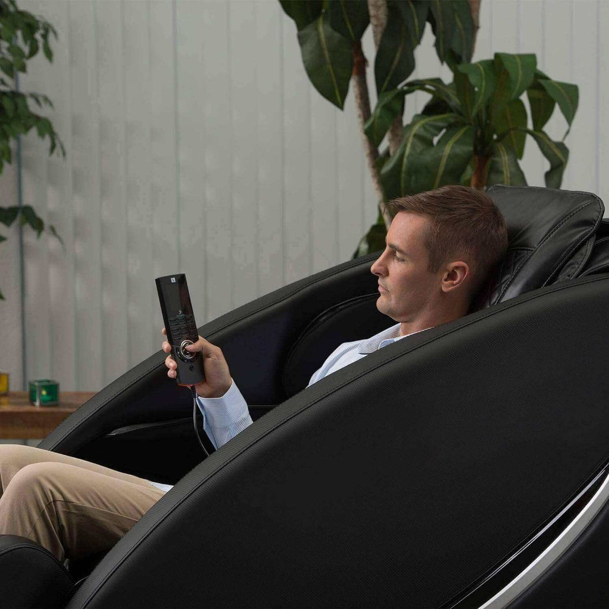 Massage chair Ji - SL Track in black synthetic leather, reclining with a man using the handheld remote