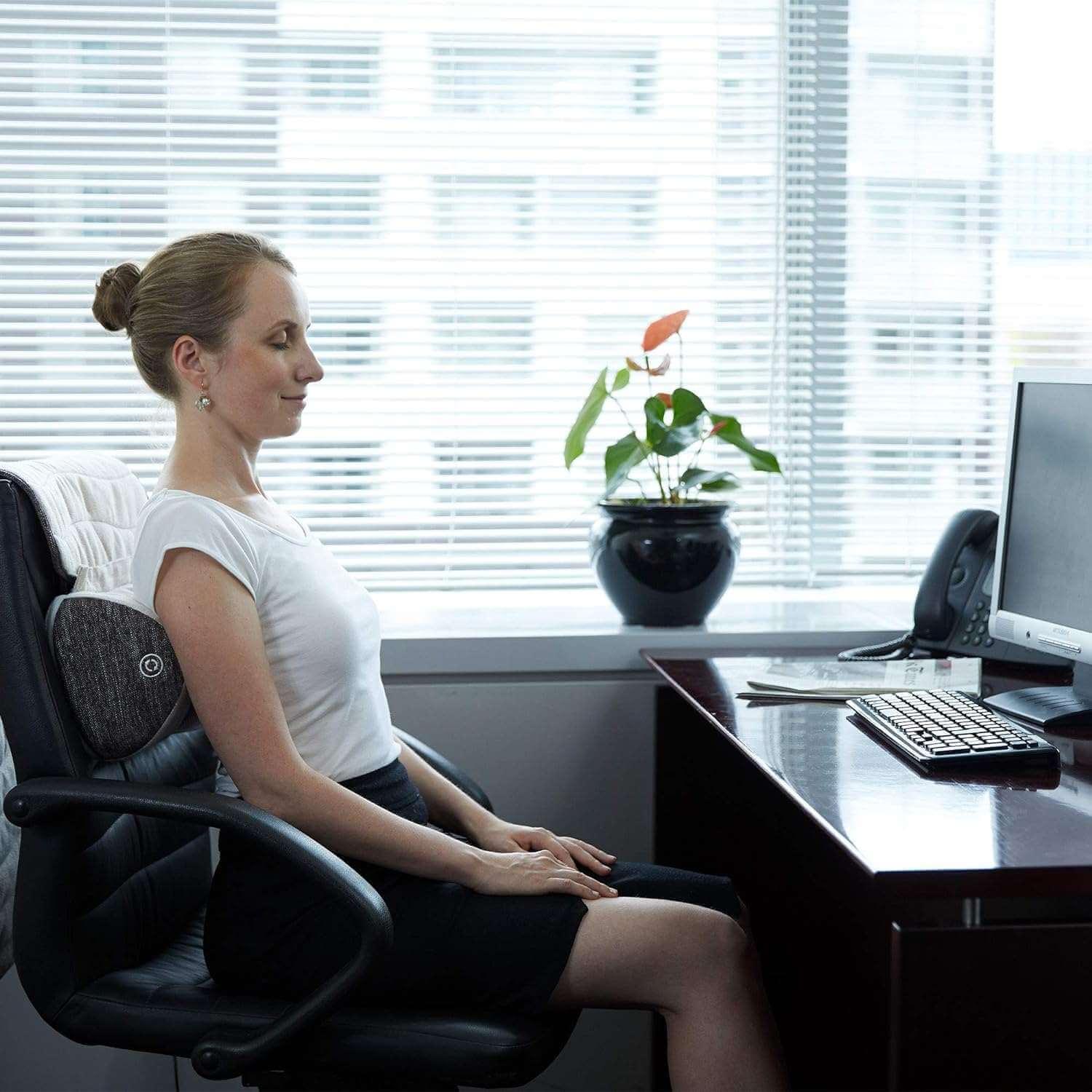 Woman sitting in office chair using Synca Wellness Lumbar Massage Cushion for back comfort
