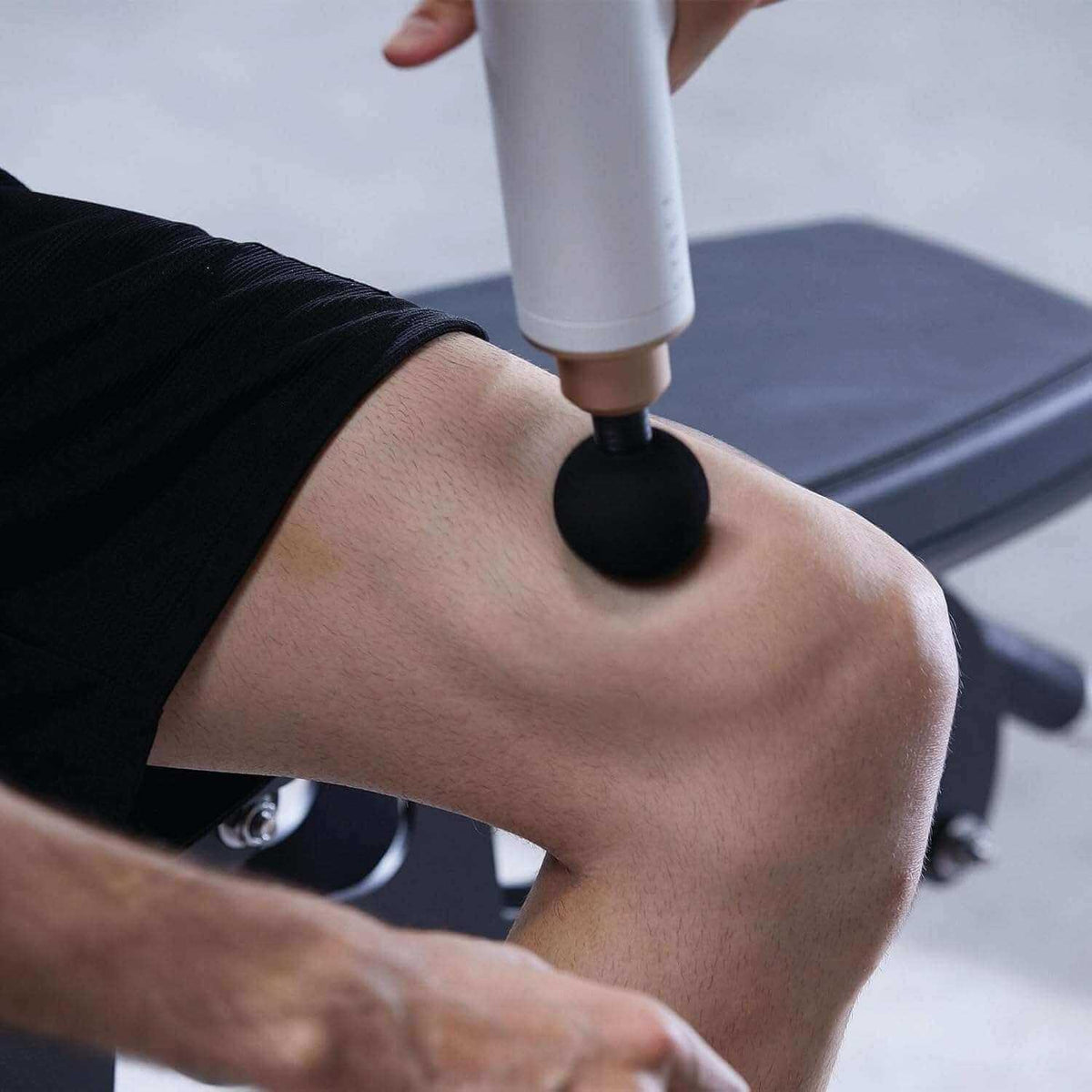 Massage Gun with a white cylindrical body and black rounded attachment being used on a bent knee