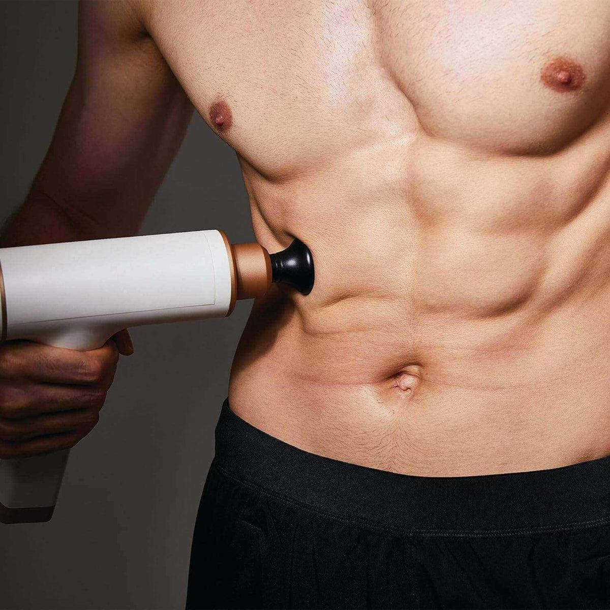 Massage Gun with a white body, copper-toned collar and black massage head pressed against a man's abdomen