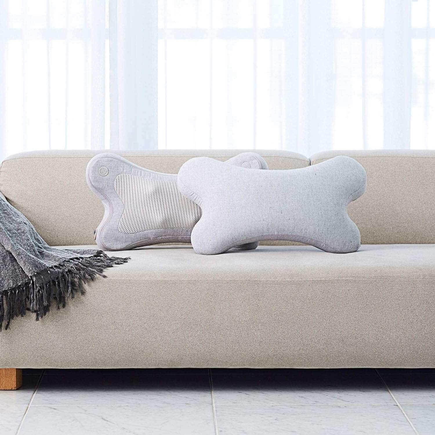 Synca Wellness portable lumbar massage pillow in light gray displayed on beige sofa