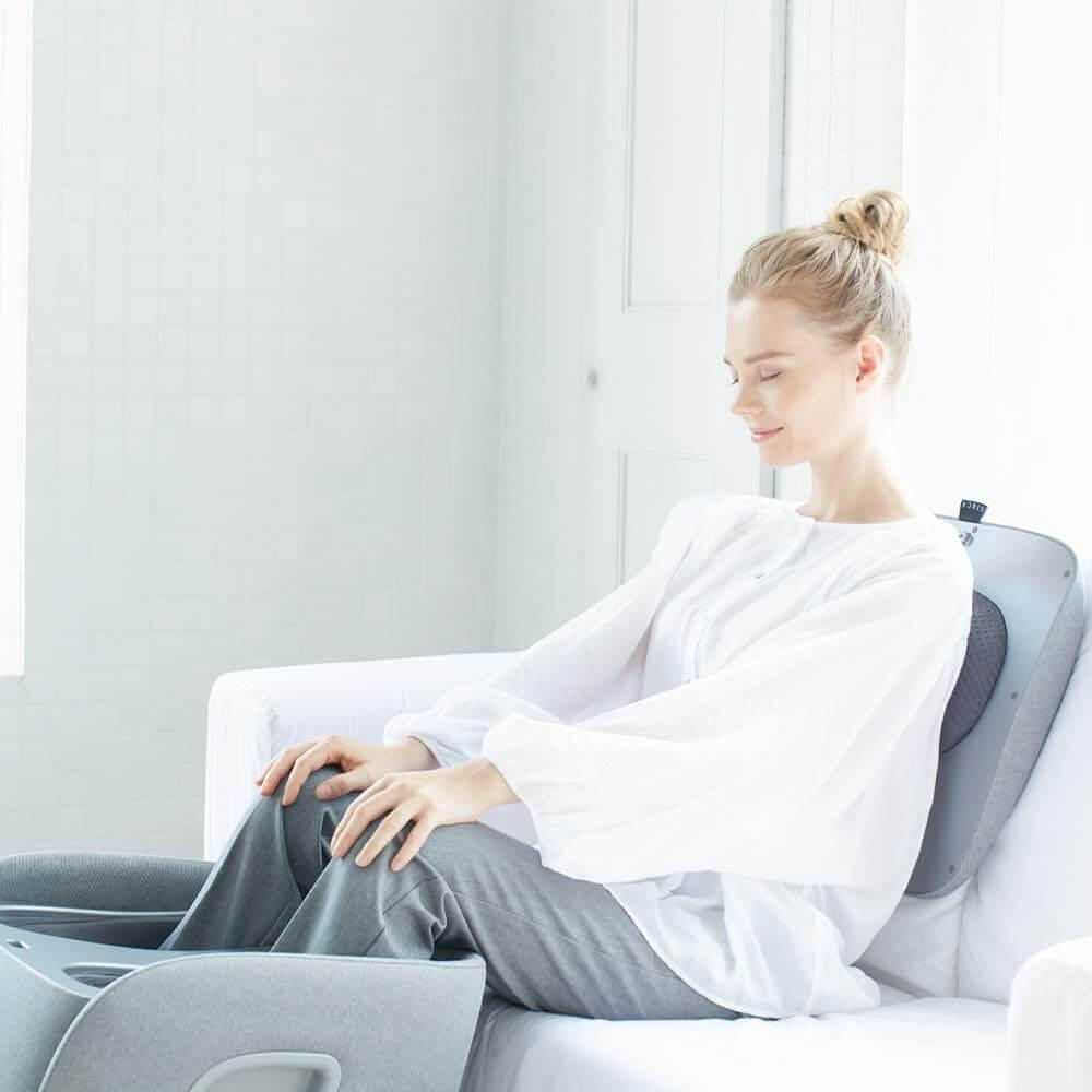Woman using Synca Wellness REI Foot Massager while sitting on a white couch at home
